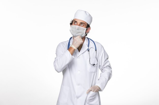 Front view male doctor in medical suit with mask as a protection from covid- thinking on white wall coronavirus virus pandemic medicine