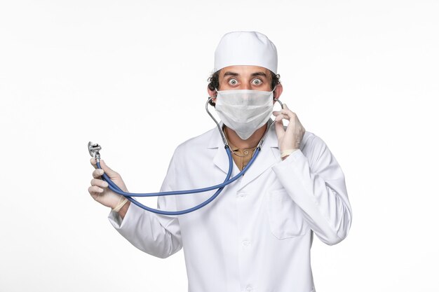 白い机のスプラッシュコロナウイルスウイルスパンデミックで聴診器を使用してcovidからの保護としてマスクと医療スーツの正面図男性医師