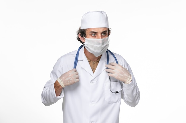Вид спереди мужчина-врач в медицинском костюме с маской в качестве защиты от covid- на белом столе коронавирусная вирусная пандемическая медицина