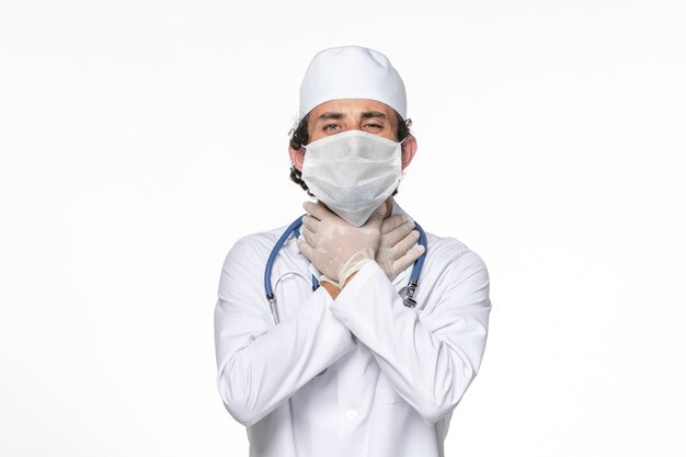 Front view male doctor in medical suit with mask as a protection from covid on white wall virus splash coronavirus pandemic