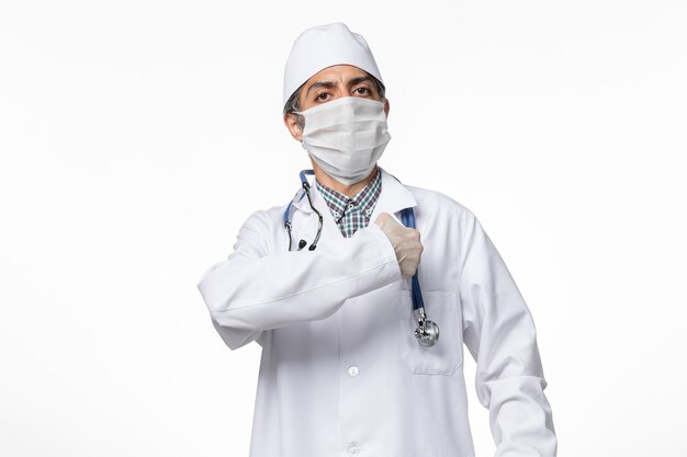 Front view male doctor in medical suit with mask due to covid- on light-white surface