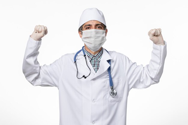 Вид спереди мужчина-врач в медицинском костюме с маской из-за covid- на светлой белой поверхности
