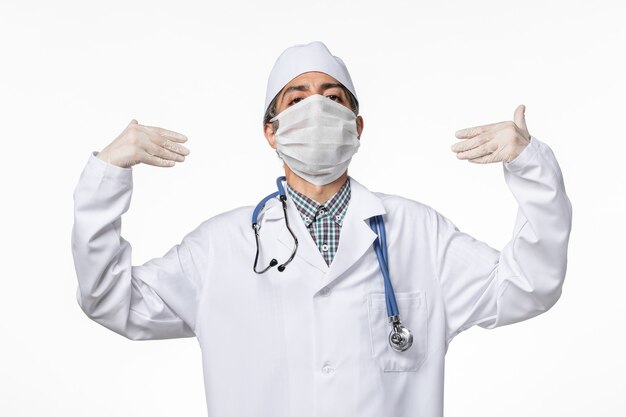 Front view male doctor in medical suit with mask due to covid- on the white surface