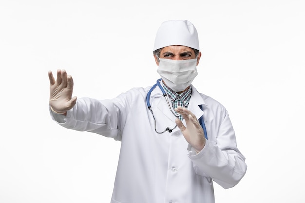 Front view male doctor in medical suit with mask due to covid- on white surface