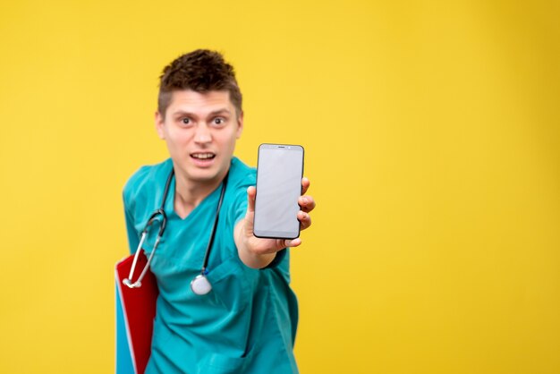 Front view of male doctor in medical suit with phone and note on the yellow wall