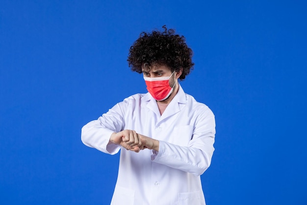 Front view male doctor in medical suit with red mask on blue background hospital virus covid- health medicine vaccine drug