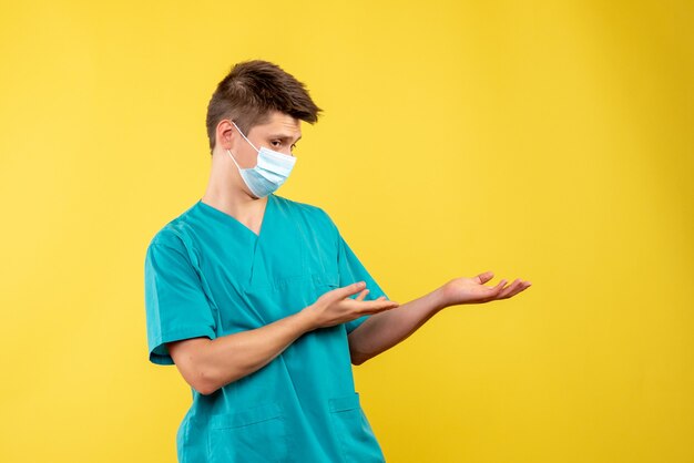 Front view of male doctor in medical suit with sterile mask on the yellow wall