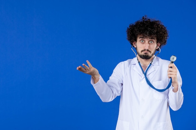 青い背景のパンデミックコビッドウイルス病院ワクチンコロナウイルス薬にステソスコープで医療スーツを着た男性医師の正面図