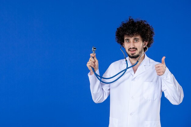 Front view of male doctor in medical suit with stethoscope on blue surface