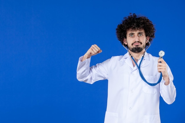 Front view of male doctor in medical suit with stethoscope on blue surface