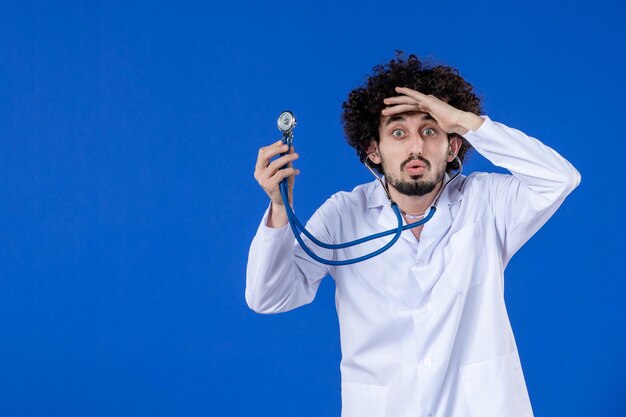 Front view of male doctor in medical suit with stethoscope on blue surface