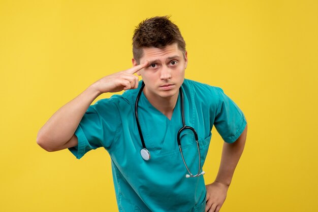 Front view of male doctor in medical suit with stethoscope on his neck on yellow wall