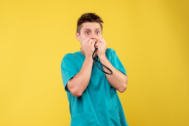 Front view of male doctor in medical suit with stethoscope scared on yellow wall