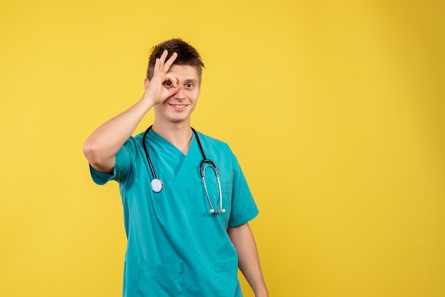 Front view of male doctor in medical suit with stethoscope on a yellow wall