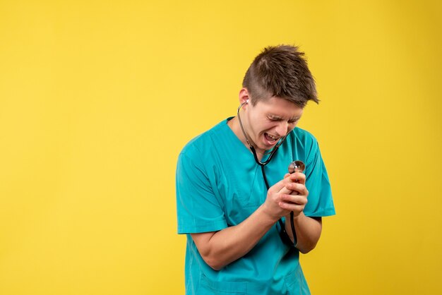 Front view of male doctor in medical suit with stethoscope on a yellow wall