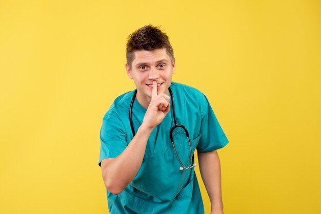 Front view of male doctor in medical suit with stethoscope on a yellow wall