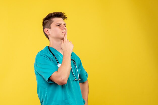 Front view of male doctor in medical suit with stethoscope on yellow wall