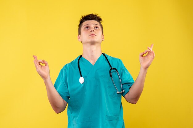 Front view of male doctor in medical suit with stethoscope on yellow wall