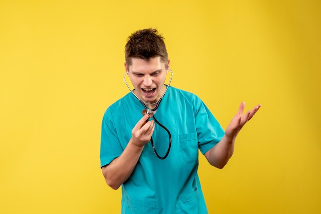 Вид спереди мужчины-врача в медицинском костюме со стетоскопом на желтой стене