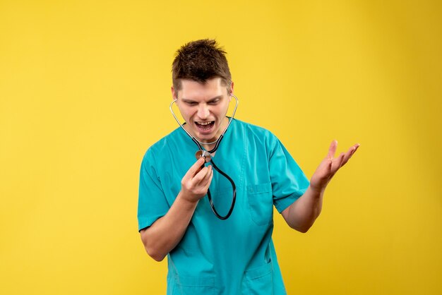 Front view of male doctor in medical suit with stethoscope on yellow wall