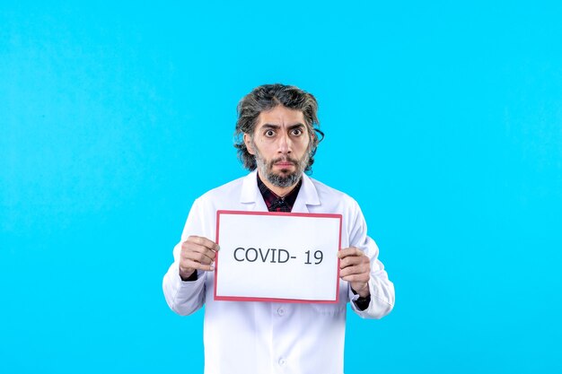 Front view male doctor in medical uniform holding covid- writing on the blue