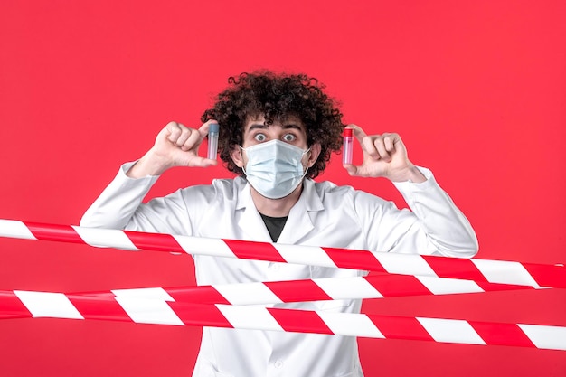 Врач-мужчина в медицинской форме, вид спереди, держит фляги на красном фоне, цвет карантина, изоляция, предупреждение об опасности для здоровья