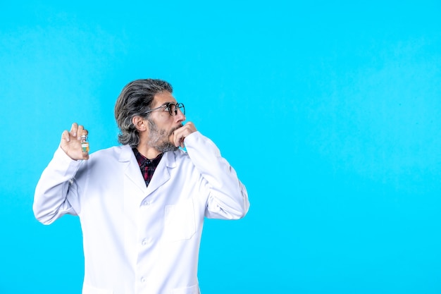 Front view male doctor in medical uniform holding little flask on blue