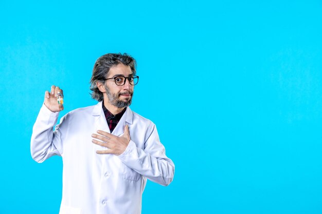 Front view male doctor in medical uniform holding little flask on blue