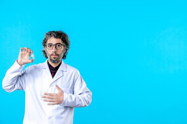 Front view male doctor in medical uniform holding little flask on blue