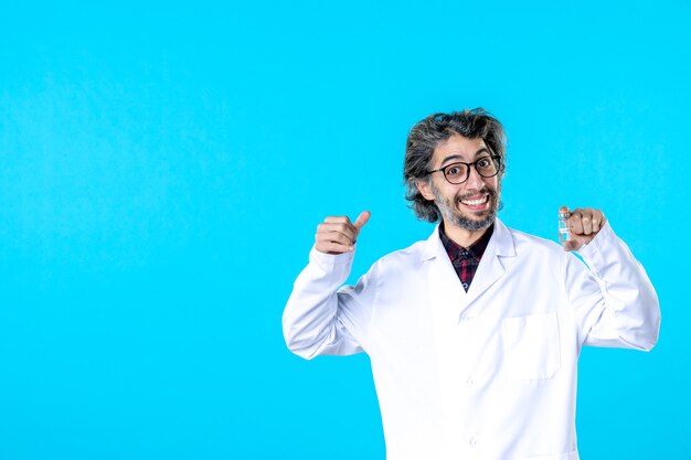 Front view male doctor in medical uniform holding little flask on blue