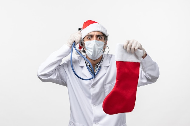 Бесплатное фото Вид спереди мужчина-врач, наблюдающий за праздничным носком на белом полу, вирус covid, здоровье праздника