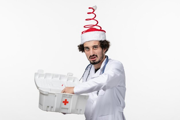 Front view of male doctor opening first aid kit on a white wall