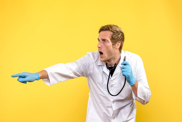 Вид спереди мужской доктор, указывая на что-то на желтом фоне, вирус здоровья, медик, эмоция