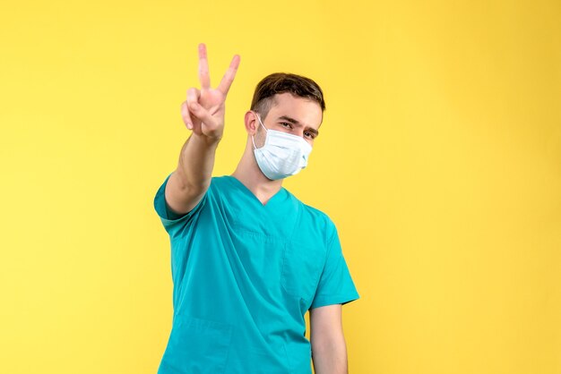 Front view of male doctor posing in mask on yellow wall