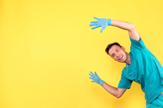 Front view of male doctor posing with blue gloves on yellow wall