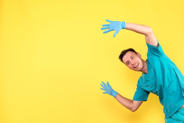 Вид спереди мужчины-врача, позирующего с синими перчатками на желтой стене