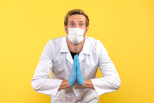 Front view male doctor in praying pose on yellow background pandemic medic health covid-