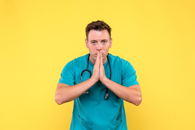 Front view of male doctor praying on yellow wall