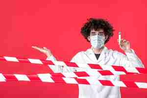 Бесплатное фото Врач-мужчина, вид спереди, готовит инъекцию против вируса на красном фоне, предупреждая о коронавирусной медицинской карантинной больничной форме