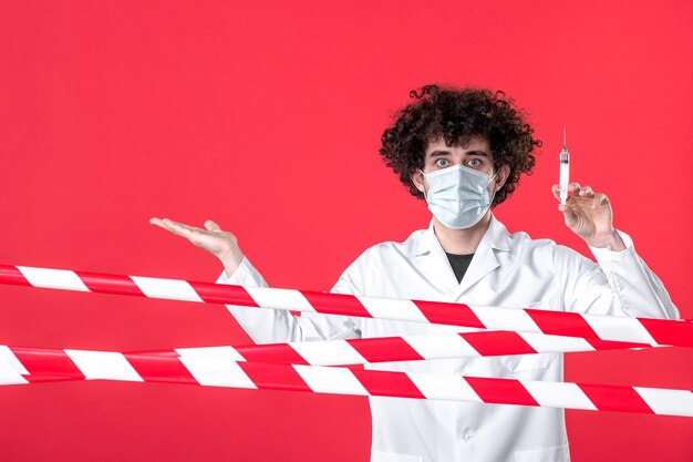 正面図赤い背景のウイルスに対する注射を準備している男性医師警告covid-健康医療検疫病院の制服