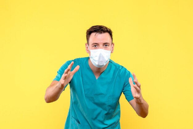 Front view of male doctor in protective mask on yellow wall