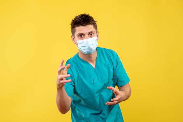 Front view of male doctor in protective mask on a yellow wall