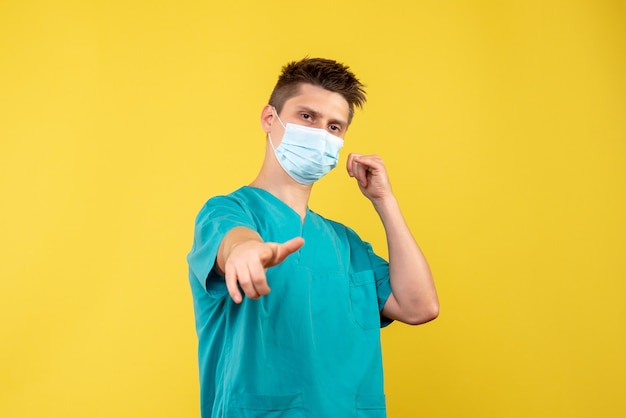 Front view of male doctor in protective mask on yellow wall