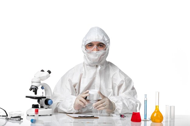 Вид спереди мужчина-врач в защитном костюме держит пустую фляжку и пишет на белом столе