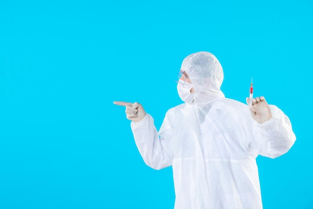 Вид спереди мужчина-врач в защитном костюме, держащий инъекцию на синем