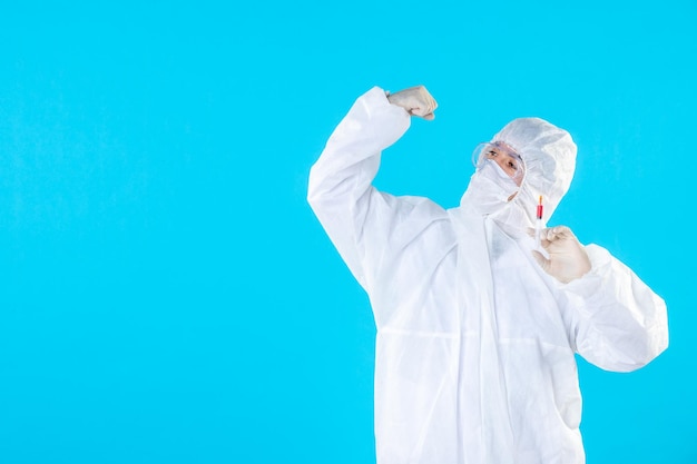 Front view male doctor in protective suit holding injection on blue