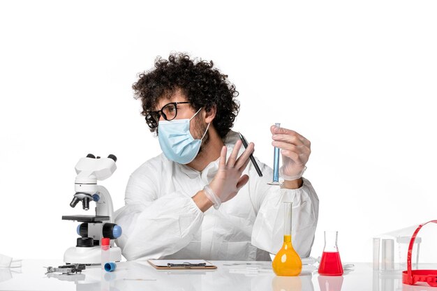 Вид спереди мужчина-врач в защитном костюме и маске, держащий колбу с синим раствором на светлом белом фоне, пандемический вирус эпидемии коронавируса