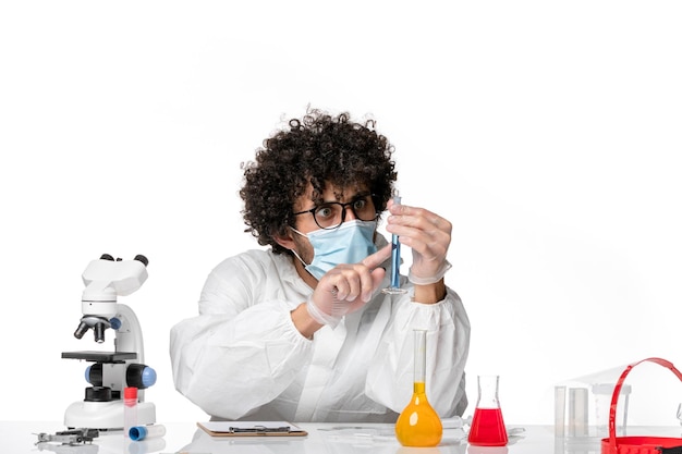 Front view male doctor in protective suit and mask holding flask with blue solution on a white background pandemic covid- epidemic virus