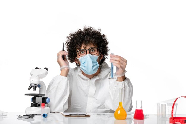 保護スーツと白い机の上の青い溶液でフラスコを保持しているマスクの正面図男性医師パンデミックコビデミックウイルス