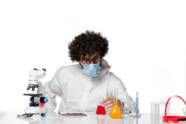 Front view male doctor in protective suit and mask holding flask with red solution on light-white background pandemic covid- epidemic virus